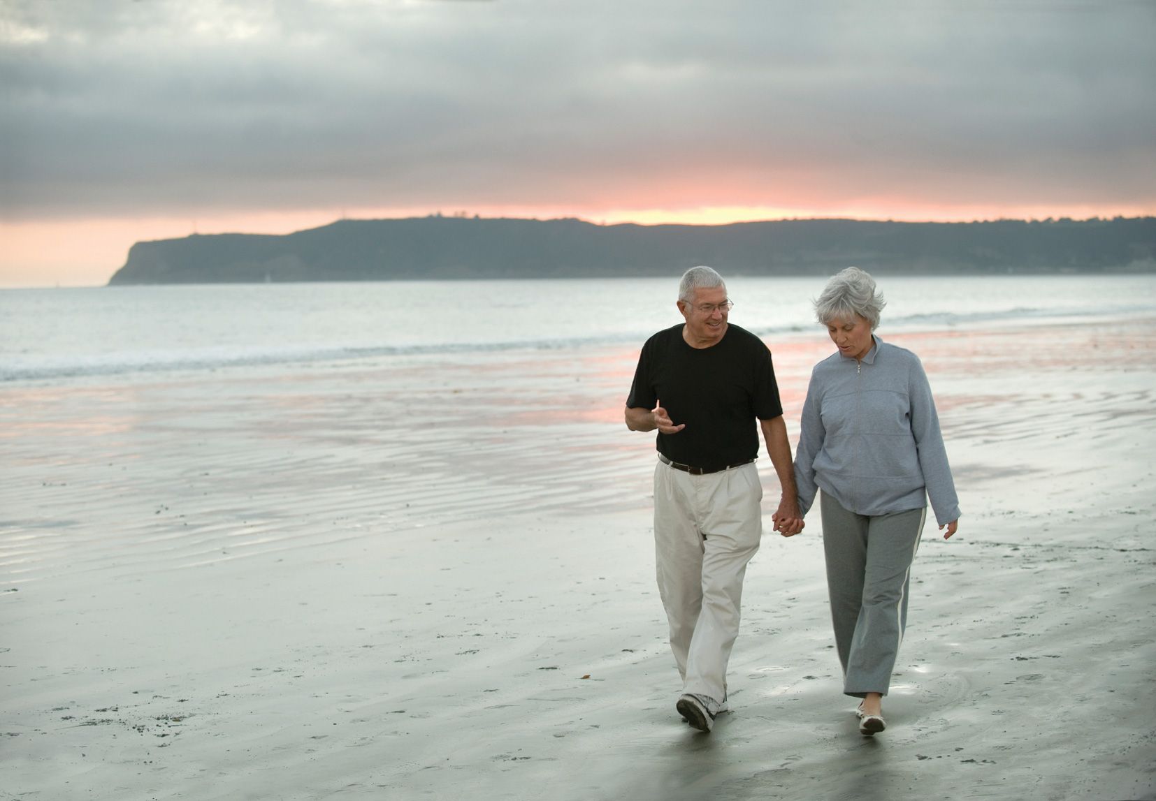 Picture of an older couple walking hand in hand on a beach.