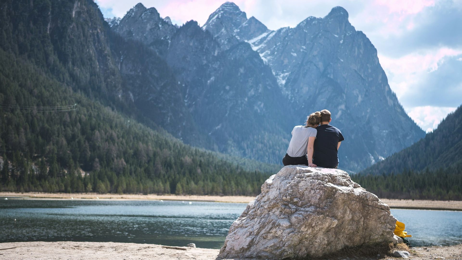 Couple sitting on a rock in front of a lake with huge mountains in backdrop